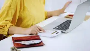 Mujer usando calculadora y portátil para gestionar sus finanzas como autónomo.