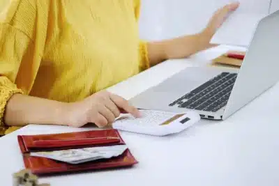 Mujer usando calculadora y portátil para gestionar sus finanzas como autónomo.