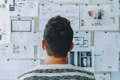 Trabajador autónomo observando un panel lleno de notas y diagramas para planificar un proyecto.