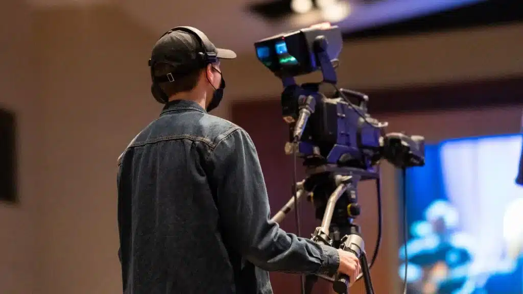 Persona con auriculares y gorra operando una cámara de vídeo profesional en un plató.