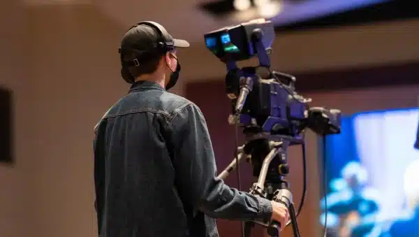 Persona con auriculares y gorra operando una cámara de vídeo profesional en un plató.