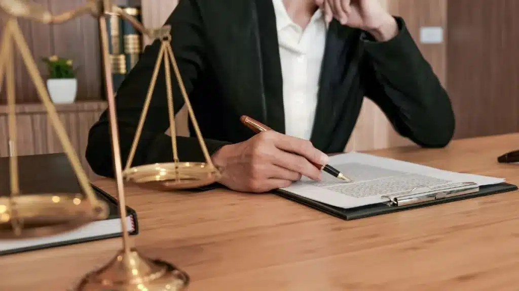 Persona vestida formalmente revisando un documento legal sobre una mesa de despacho.