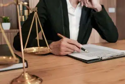 Persona vestida formalmente revisando un documento legal sobre una mesa de despacho.